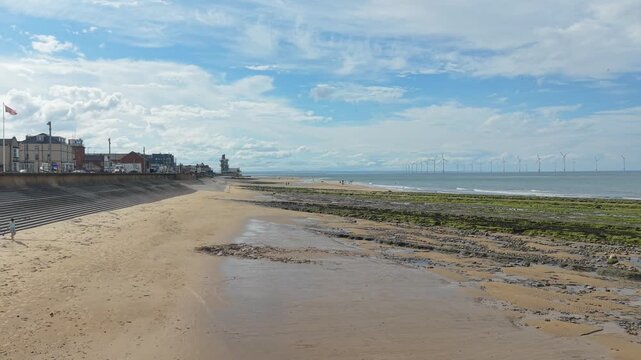 ​Panoramic view of Redcar Rocks or Salt Scars coastline with rocky beach, sea wall, and distant wind farm, 
