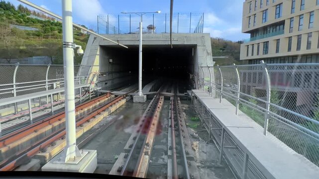 View from front wagon of a driverless metro train entering a tunnel from an open section in Istanbul. Automated urban rail transit with modern infrastructure and city transport on a cloudy day