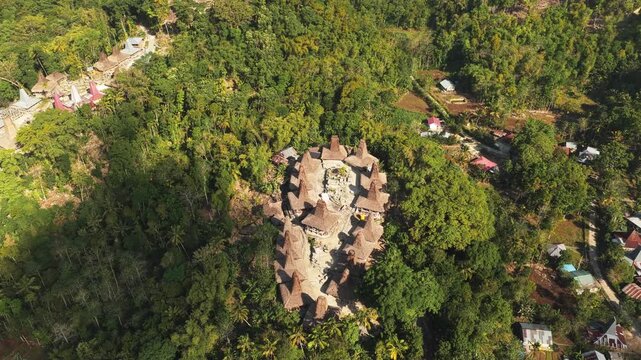 Aerial view of Kampung Prai Ijing, a traditional village with distinctive thatched-roof houses nestled in a lush green forest landscape in Kota Walkabubak, East Nusa Tenggara, Indonesia.