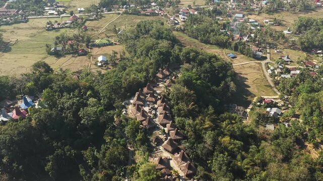Aerial view of Kampung Prai Ijing with its traditional thatched-roof houses nestled among lush green hills and trees in Kota Walkabubak, East Nusa Tenggara, Indonesia.