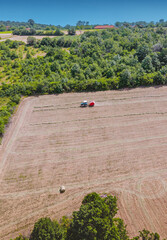 Fototapeta premium Tractor forming hay bales in a dry rural field from an aerial perspective. Agricultural activity during summer harvest