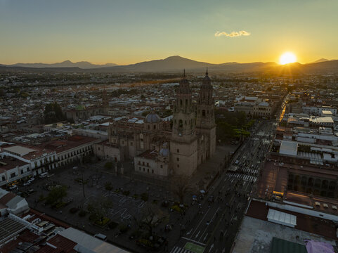 Aerial view of the historic Morelia Cathedral illuminated by the golden hour sunset, surrounded by colonial architecture and urban streets in Morelia, Michoacan, Mexico.