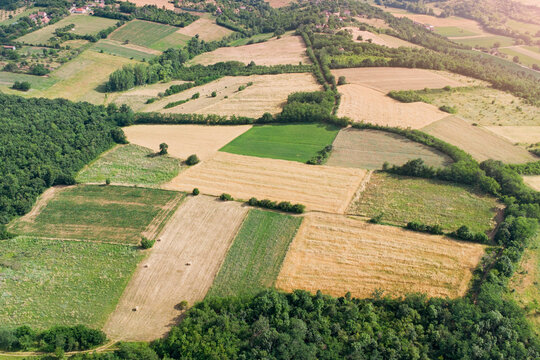 Warm golden summer light bathes a patchwork of rolling farmland and a small village nestled among wooded hills. Rural Europe concept.