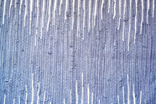 Close-up macro background of a handmade woven fabric rug featuring a textured pattern with vertical rows of blue and white threads.