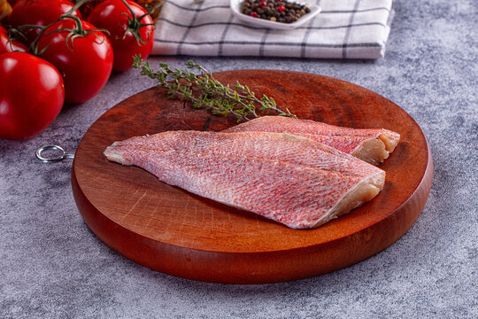 Raw sea perch fillets on wooden cutting board with fresh tomatoes and thyme
