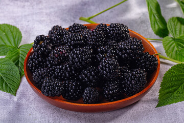 Naklejka premium Fresh blackberries in wooden bowl with green leaves on gray background