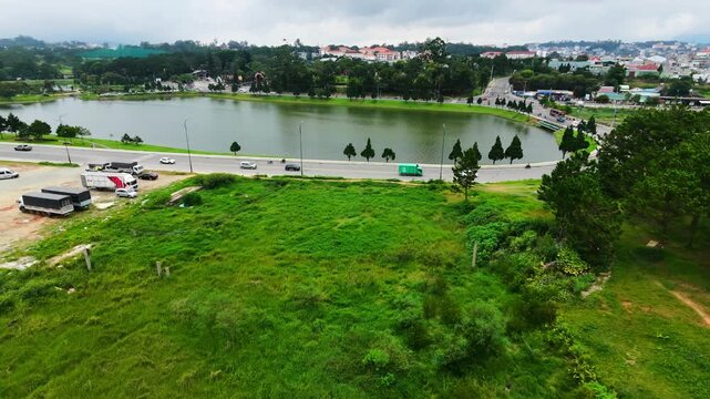 Aerial pan of cars moving alongside treelined lakeside road in urban park