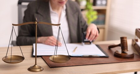 Professional lawyer working at wooden table in office, focus on scales of justice