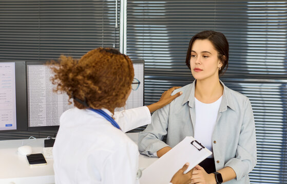 Doctor patient consultation with support empathy. A physician reassures a woman with a shoulder touch during diagnosis in clinic at a healthcare appointment. Strong message of supportive care.