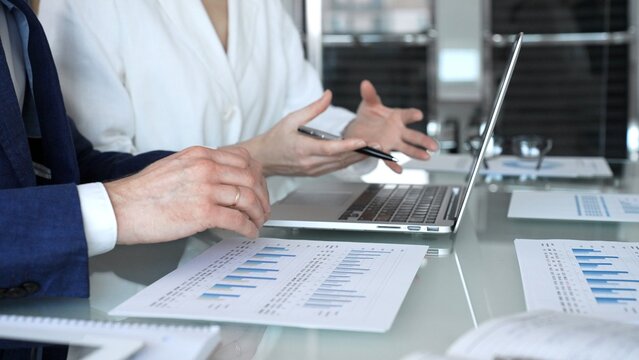 Business professionals in a meeting analyze financial charts and reports on a laptop and documents, pointing at data while planning investment strategy and growth in a modern office