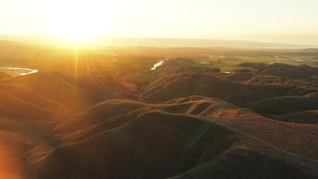Aerial view of Tanau Hills with rolling golden landscape and winding paths at sunset in Kecamatan Kambera, Nusa Tenggara Timur, Indonesia.