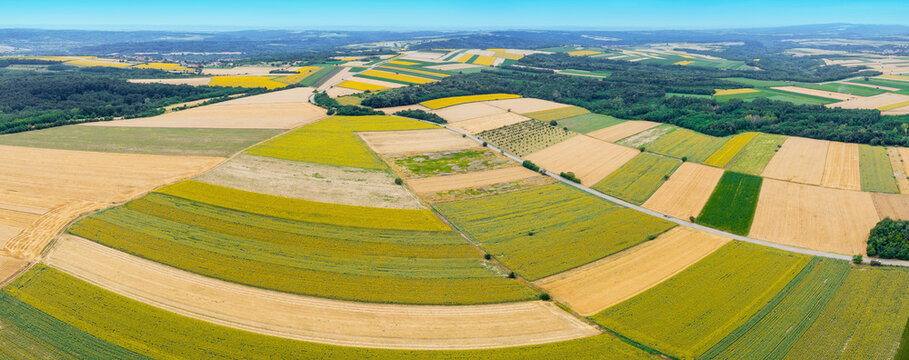Varied agricultural fields viewed from above, displaying a patchwork of green, yellow, and brown crops under a blue sky