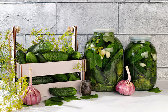 Cucumbers in a basket with dill, garlic, pickling leaves, and pickled cucumbers in jars on a kitchen counter. Harvest concept. Homemade pickle recipe and ingredients. Home canning concept.