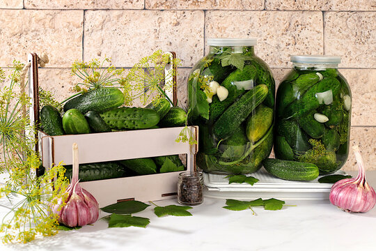Cucumbers in a basket with dill, garlic, pickling leaves, and pickled cucumbers in jars on a kitchen counter. Harvest concept. Homemade pickle recipe and ingredients. Home canning concept.