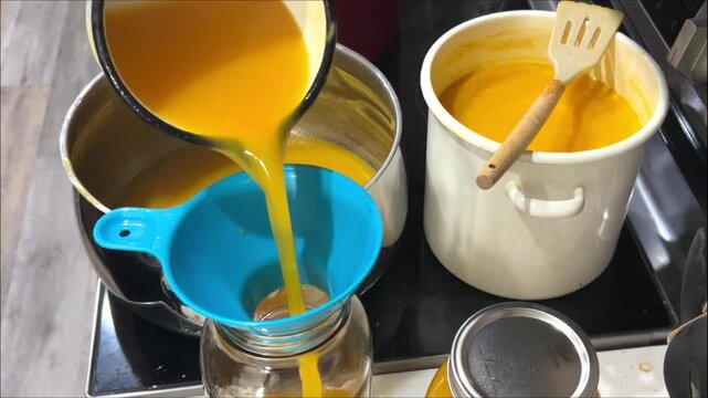 Homemade peach juice poured through a blue funnel into a glass jar in a kitchen, fruit canning, healthy beverage, summer preservation, traditional recipe.