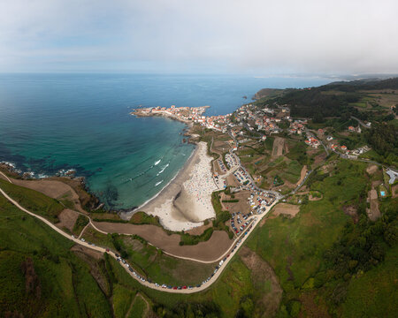 Aerial view of the coastal town of Caion featuring a sandy beach, turquoise Atlantic waters, and surrounding green fields in Caion, A Coruna, Spain.