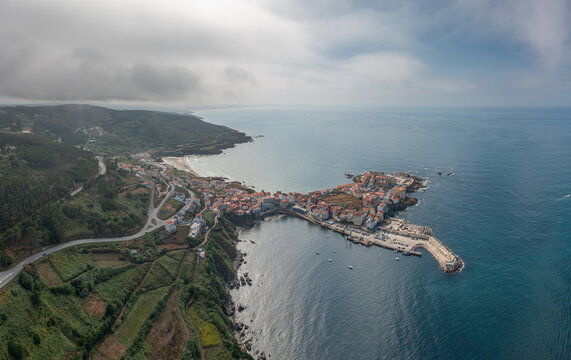 Aerial view of the coastal town of Caion with its harbor, breakwater, and surrounding green hills along the Atlantic coastline in Caion, A Coruna, Spain.