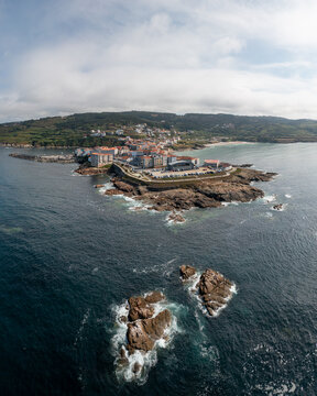 Aerial view of the coastal town of Caion with its harbor, rocky shoreline, and buildings situated on a peninsula in Caion, A Coruna, Spain.