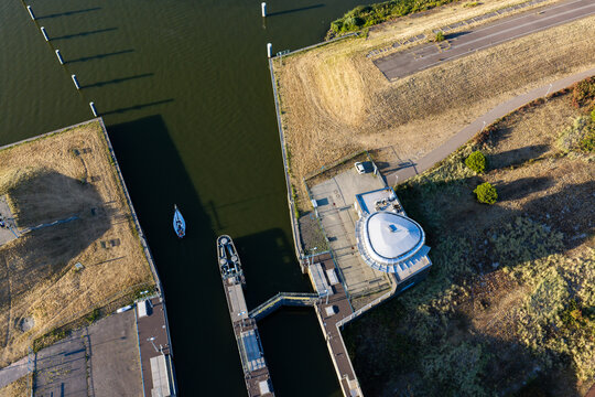 Aerial view of Naviduct Krabbersgat with a small sailboat navigating the lock system surrounded by grassy embankments and calm water in Enkhuizen, North Holland, Netherlands.