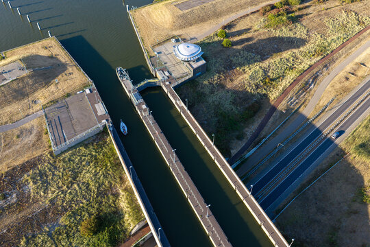 Aerial view of Naviduct Krabbersgat with a small sailboat navigating the lock system surrounded by grassy embankments and calm water in Enkhuizen, North Holland, Netherlands.
