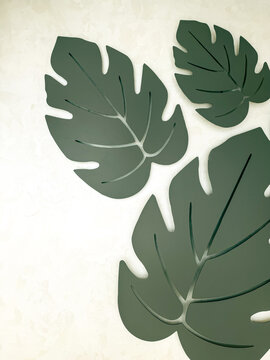 Modern decorative monstera leaf wall art in neutral gray tones on a textured light background, minimalist botanical interior decor with abstract tropical leaf shapes.