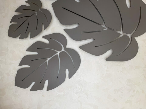 Modern decorative monstera leaf wall art in neutral gray tones on a textured light background, minimalist botanical interior decor with abstract tropical leaf shapes.