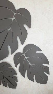 Modern decorative monstera leaf wall art in neutral gray tones on a textured light background, minimalist botanical interior decor with abstract tropical leaf shapes.