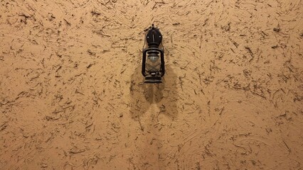 Vintage black lantern hanging on traditional mud wall with straw texture. © mohamed alhamami