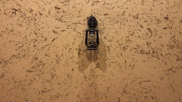 Vintage black lantern hanging on traditional mud wall with straw texture.