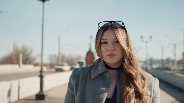 Charming woman capturing scene on bridge. Graceful woman in vintage coat preparing to film outdoors. Refined lady with long hair and vintage attire filming confidently on bridge at sunset