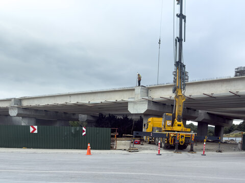 View of a construction site featuring a large yellow crane and a worker standing on a concrete bridge structure under a cloudy sky in Sariyer, Istanbul, Turkiye.