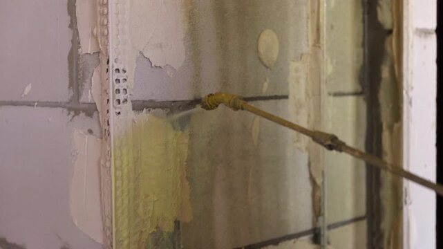 Worker applying primer to wall with spray gun during renovation