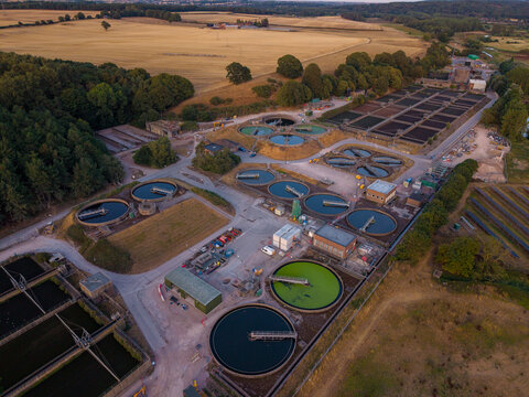 Aerial view of Brancote wastewater treatment plant with circular sedimentation tanks and industrial infrastructure surrounded by fields and trees in Stafford, England, United Kingdom.