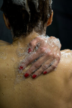 Detailed close-up of a hand with red nail polish spreading soap bubbles across a wet back in the shower.
