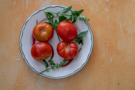 Fresh garden tomatoes, basil sprigs and red chillies displayed on a plate against a rustic ochre tabletop