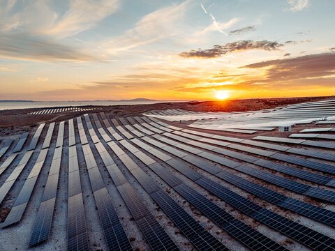 View of a large solar power plant with rows of photovoltaic panels on rocky terrain under a golden sunset sky in Novalja, Lika-Senj County, Croatia.