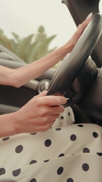 Close-up of a woman in a polka dot dress confidently gripping the steering wheel while driving her car. Vertical video