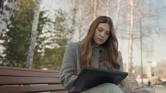 Woman drawing on tablet outside. Relaxed artist sketching on tablet amidst natural surroundings. Engaged woman illustrating with stylus on tablet in peaceful outdoor setting during winter