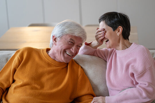 Positive carefree senior husband and wife laughing and joking while resting together at home on sofa, cheerful smiling elderly couple on couch, happiness and connection, harmony in aged partnership.