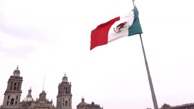 Massive Mexican flag waving in front of the historic Metropolitan Cathedral in Mexico City.