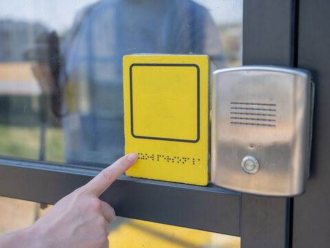 A blind woman reads the braille sign next to a call button.