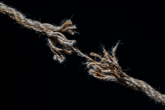 Fraying rope under tension on black background, closeup. Frayed brown rope about to break under pressure concept of stress tension risk and limit or breaking point