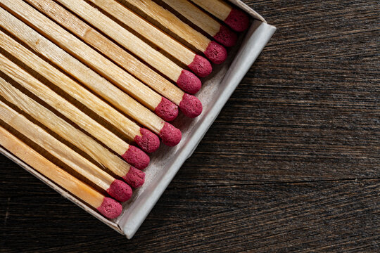 Open matchbox with wooden matches on dark wooden surface. Top view closeup of unused wooden matches with pink heads inside cardboard box placed on rustic wood background