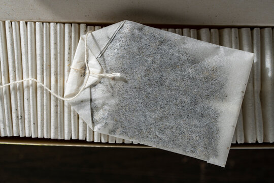 Paper tea bag on top of row in open box. Top view closeup of single white tea bag with string lying horizontally on neatly packed row of paper tea bags inside cardboard container