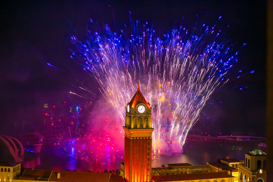 Intense blue and white fireworks exploding above the historic clock tower in Sunset Town, Phu Quoc. Night celebration.
