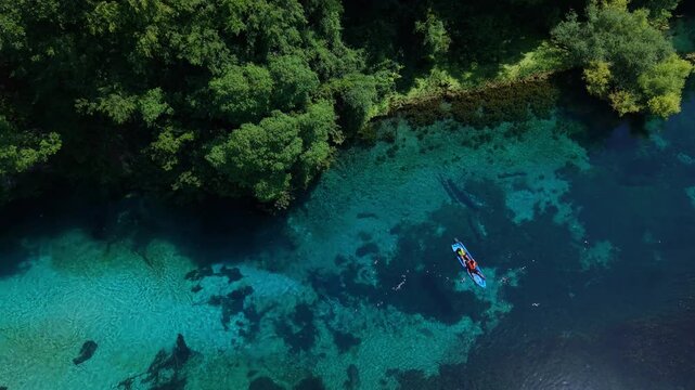 Aerial view of a person kayaking on the crystal clear blue waters of The Blue Eye spring surrounded by lush green trees in Saranda, Qarku i Vlores, Albania.