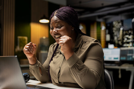 Excited African American woman reacts with satisfaction after receiving a contract deal, celebrating a professional breakthrough and new opportunity in the office after hours at night.