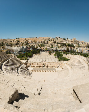 View of the Roman Theater with its ancient stone seating and stage area, set against the urban skyline of Amman, Amman Governorate, Jordan.