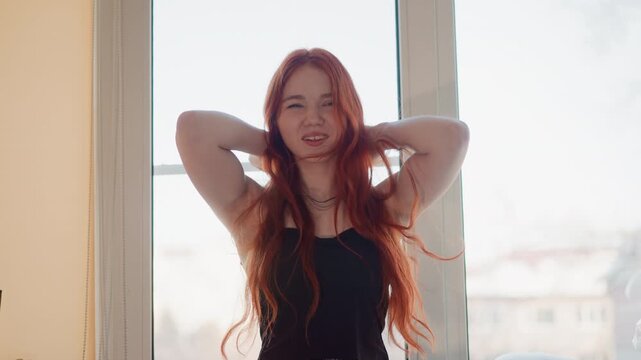 Reflective woman near window. Quiet morning scene of redheaded woman practicing lyrics. An intimate portrayal of contemplative redhead woman working through song lyrics in soft morning light