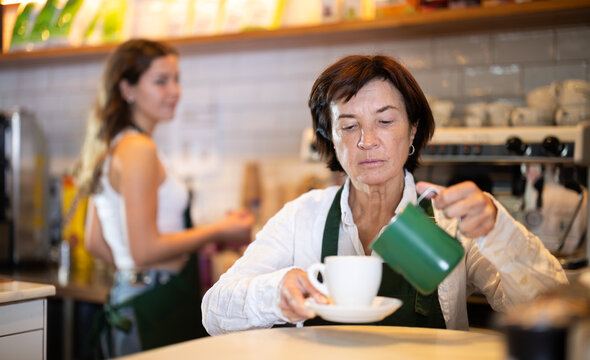 Elderly woman barista pouring freshly brewed coffee into cup in cafe